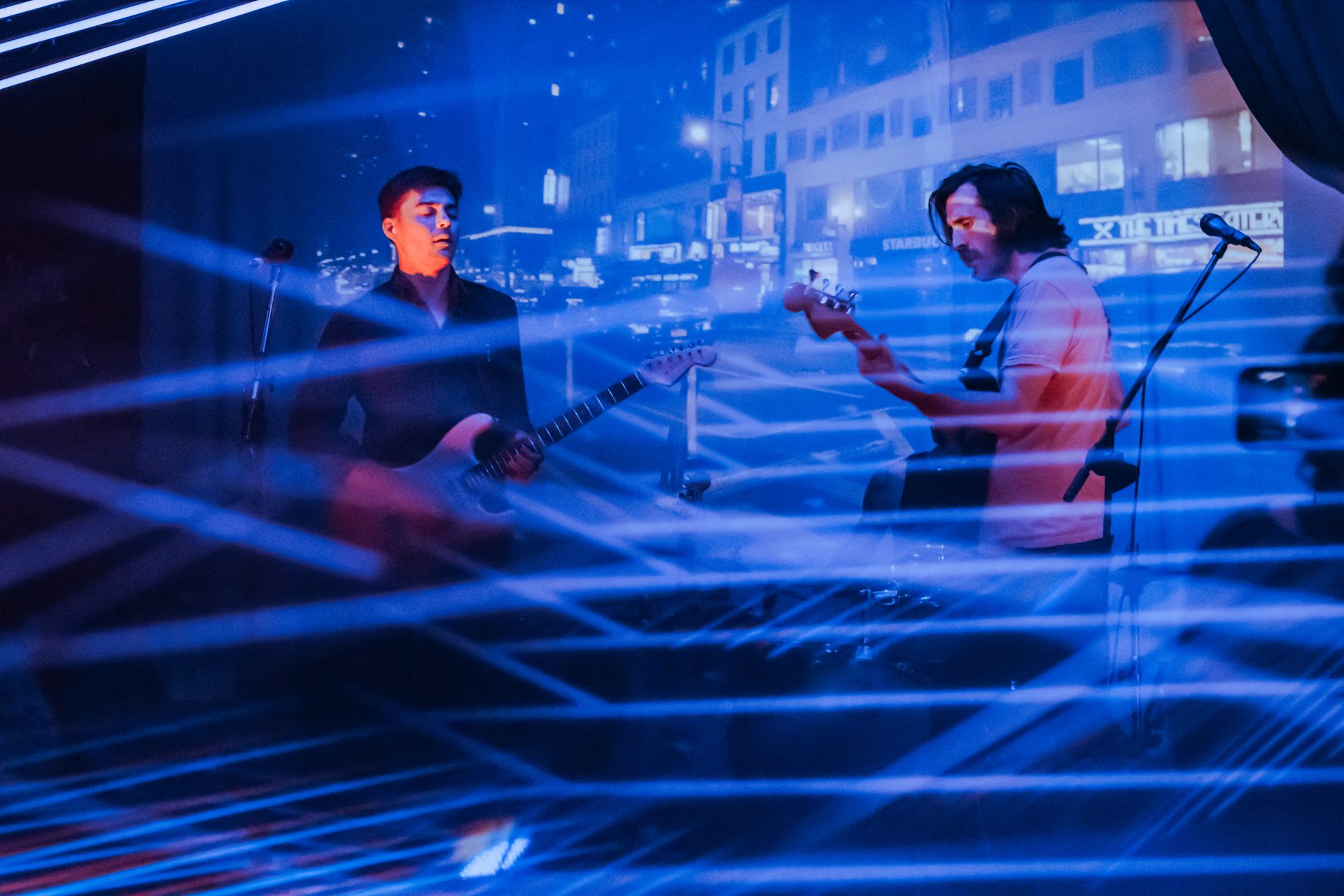 Two guitarists performing on stage with blue laser beams cutting through the dark