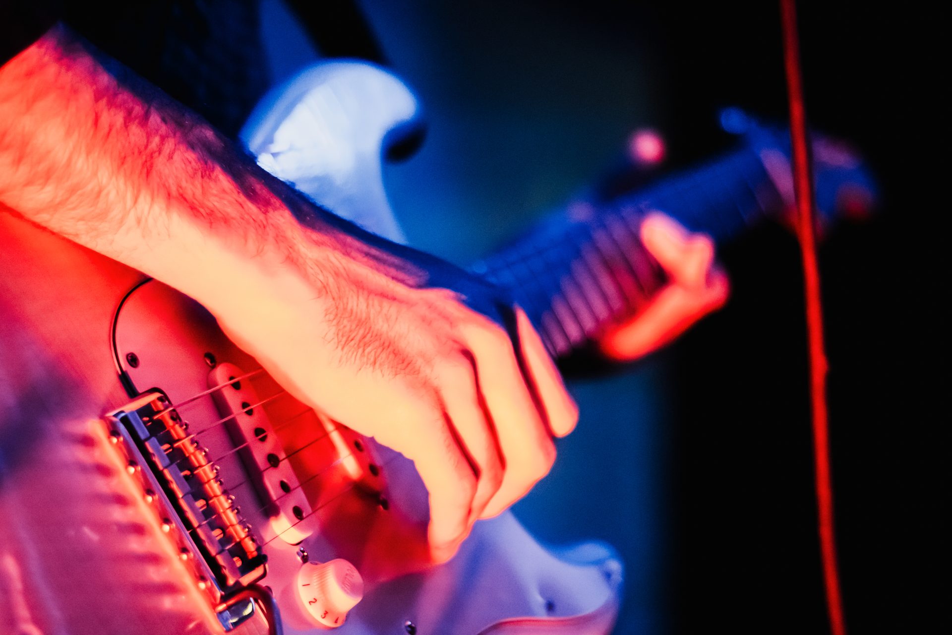 Close-up of guitarist's hands on Stratocaster under red and blue stage lights