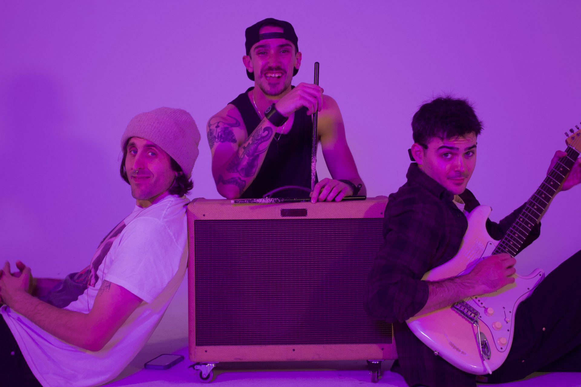 Caught Feelings — three band members casually posed around a guitar amp in purple light